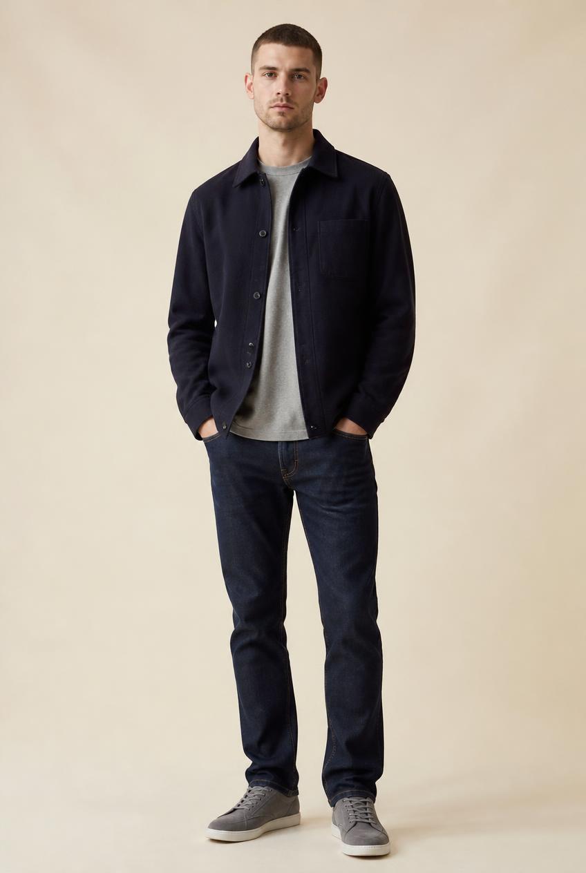 Man in a navy wool overshirt, grey tee, indigo jeans and grey suede sneakers, head to toe.