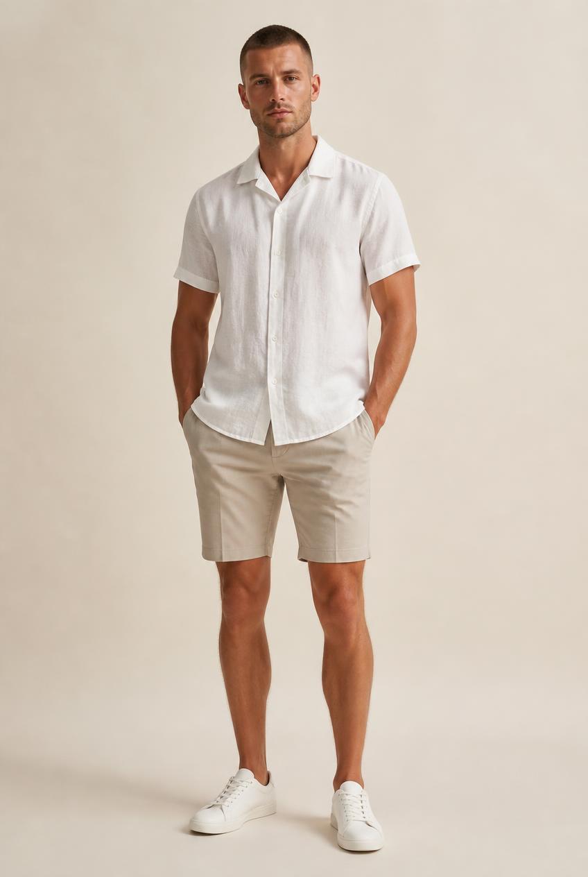 Man in a white short-sleeve linen shirt, stone tailored shorts and white leather sneakers, head to toe.